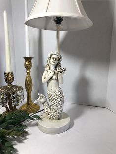 a lamp that is next to a mermaid figurine and some candles on a table