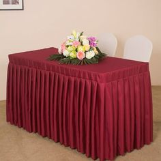 the table is covered with a red cloth and flowers in front of a white chair