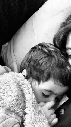 a black and white photo of a young boy sleeping with his head on a woman's shoulder