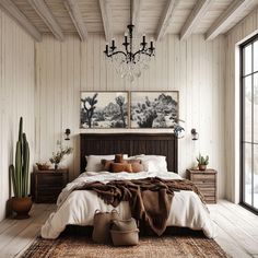 a bedroom with white walls and wood flooring has a large bed, chandelier, potted plants, and two paintings on the wall