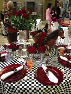 the table is set with red plates, silverware and flowers in vases on it