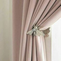 a curtain with a bee on it hanging in front of a window covered by pink drapes