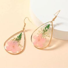 a pair of earrings with pink flowers and green leaves on the inside, hanging from gold plated hooks