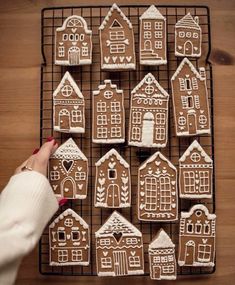 a woman is decorating gingerbread houses with icing on a wire cooling rack