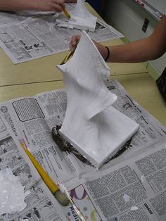 the paper is being folded on top of newspaper papers with crayons and pencils next to it