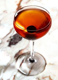 a close up of a drink in a wine glass on a marble counter top with a black dot