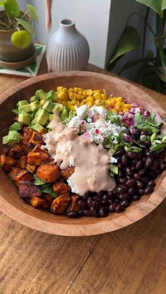 a wooden bowl filled with black beans, corn, avocado, and dressing