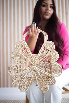 a woman sitting on a chair holding up a woven purse with intricate designs and beads