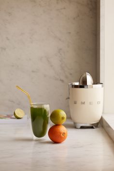 two oranges and one lime sit on a counter next to a juicer with a straw in it