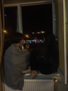 two people sitting on a window sill at night