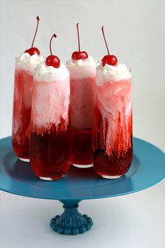 three glasses filled with ice cream and cherries on top of a blue tablecloth