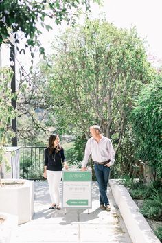 a man and woman walking down a sidewalk with a sign in front of them that says,