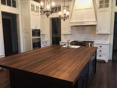 a large kitchen with an island in the middle and white cabinets on both sides is lit by chandeliers