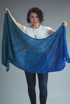 a woman holding up a blue crocheted shawl