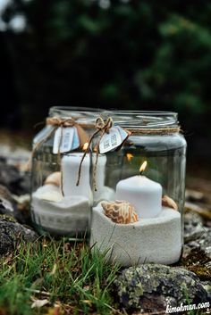 two mason jars filled with candles sitting on top of a rocky ground next to grass