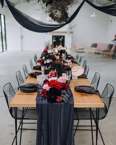 a long table is set with black and red flowers, candles, and napkins