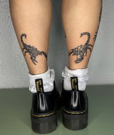 the legs and ankles of a person with tattoos on them, both wearing black rubber boots