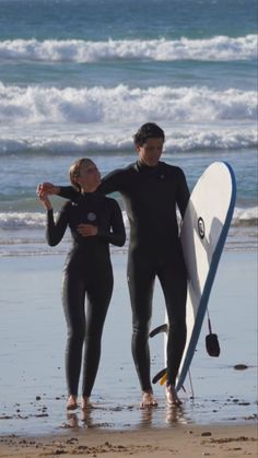 two people in wetsuits holding surfboards on the beach