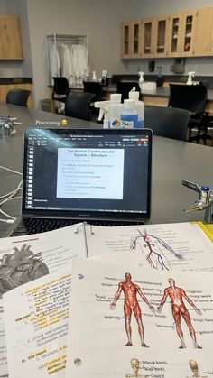 an open laptop computer sitting on top of a table next to medical diagrams and books