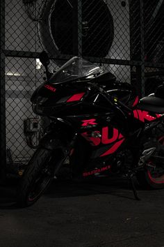 a red and black motorcycle parked in front of a chain link fence at night time