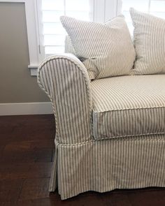 a couch with two pillows on top of it in front of a window and wooden floor