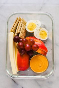 a glass container filled with fruit and crackers next to an egg, cheese, and orange juice