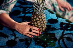 a woman's hand holding a pineapple on top of a blue tablecloth