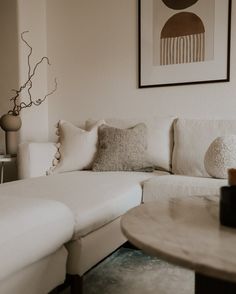 a living room with white couches and pillows on the table in front of it