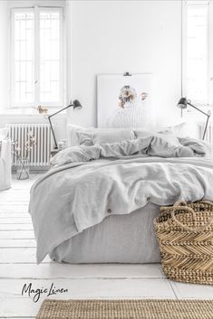 a white bedroom with grey linens and wicker baskets on the floor next to it