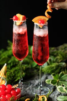 two glasses filled with red liquid and garnished with fruit