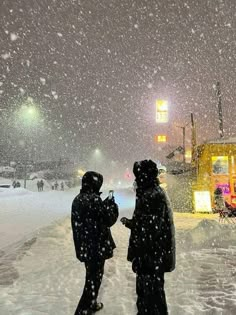 two people standing in the snow near a school bus on a snowy day at night