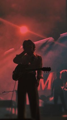 a man holding a guitar while standing in front of a stage