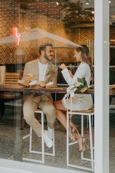 a man and woman sitting at a table in front of a glass window eating food