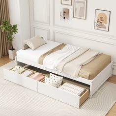 a white bed with drawers underneath it in a room next to a rug and pictures on the wall