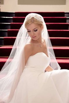 a woman in a wedding dress sitting on some steps with a veil over her head