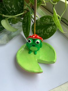 a green frog sitting on top of a leafy plant next to a potted plant