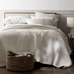 a bed with white sheets and pillows in a bedroom next to a basket on the floor