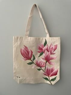 a tote bag with pink flowers painted on the front and side, hanging from a wall