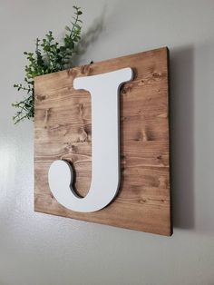 a wooden sign with the letter j on it and a plant in front of it