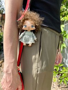 a person holding a small doll in their pocket with a red leash attached to it