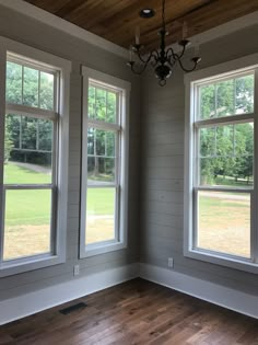 an empty room with three windows and a chandelier hanging from the wood ceiling