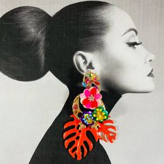 a woman wearing large earrings with flowers and leaves on the back of her ear, in front of a white background