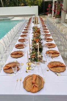 a long table is set up with place settings for dinner by the pool in front of it