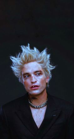 a man with blonde hair wearing a black suit and chain necklaces on his neck