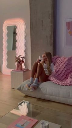 a woman sitting on top of a white couch next to a pink blanket and coffee cup