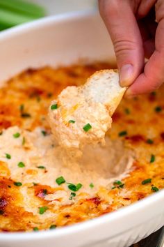 a hand dipping a piece of bread into a bowl of cheesy potato dip