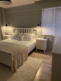 a white bed sitting in a bedroom next to a window with blinds on the windowsill