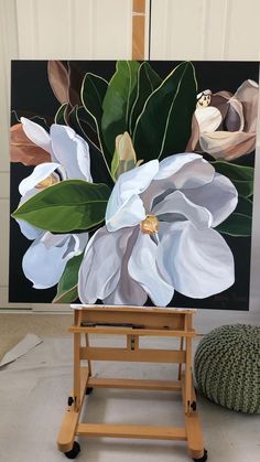 an easel with a painting on it in front of a white flower and green leaves