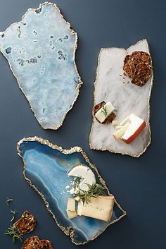 three different types of cheeses on trays with blue and white marbled surfaces