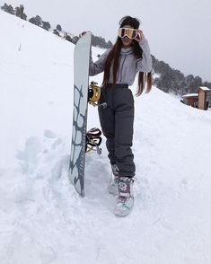 a woman standing in the snow with a snowboard on her shoulder and goggles on